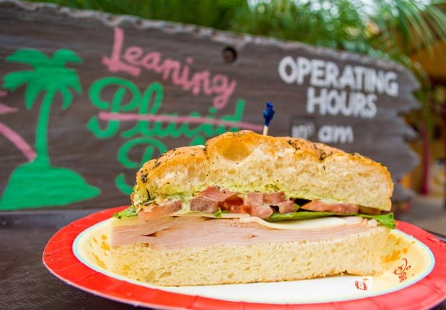 A weathered wooden sign for Leaning Palms restaurant at Disney's Typhoon Lagoon, with a sandwich pictured below the sign, styled to match the water park's shipwrecked theme